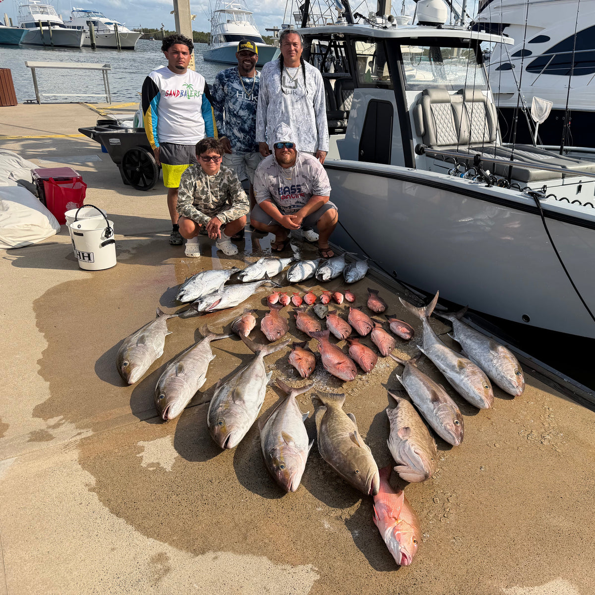 Five men posing with a large catch of various fish laid out on a concrete dock next to an Insetta  35 IFC with DMFD Life, a white boat.