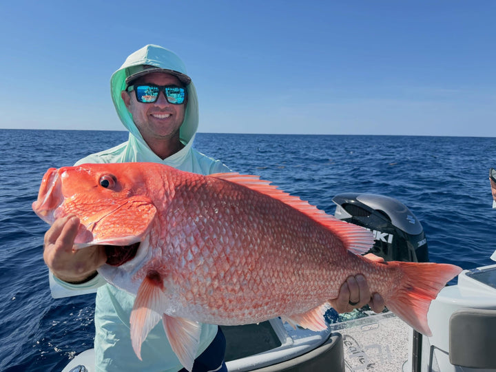 Man holding a large red fish on a Insetta 35 IFC catamaran from DMFD Life Charters  with blue water and sky in the background