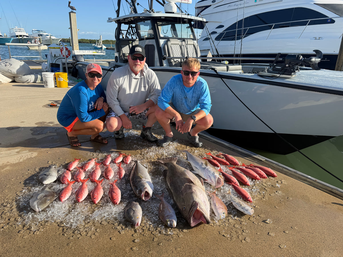 Three people crouching on a dock next to an Insetta  35 IFC with DMFD Life, with multiple caught fish arranged on ice in the foreground. This is a real outdoor environment with people present, so the subject_type is Lifestyle.