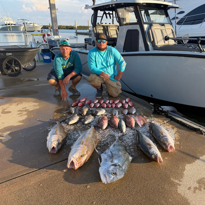 Two men crouching on a dock beside an Insetta  35 IFC with DMFD Life white boat, with multiple large fish arranged on the wet concrete in front of them. A third person is visible standing on the boat deck in the background.