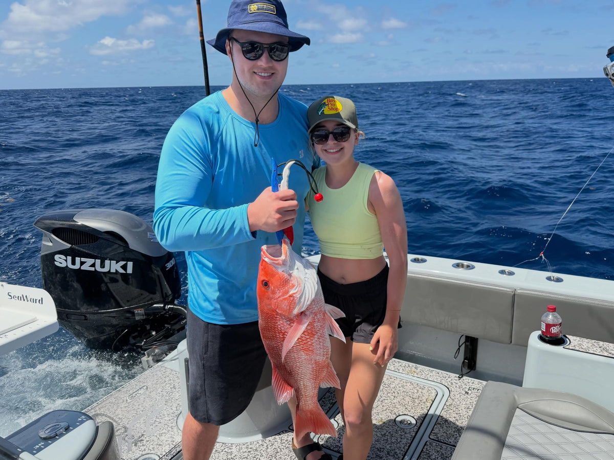 Two people on a Insetta 35 IFC catamaran from DMFD Life Charters  holding a large fish with a Suzuki motor in the background.