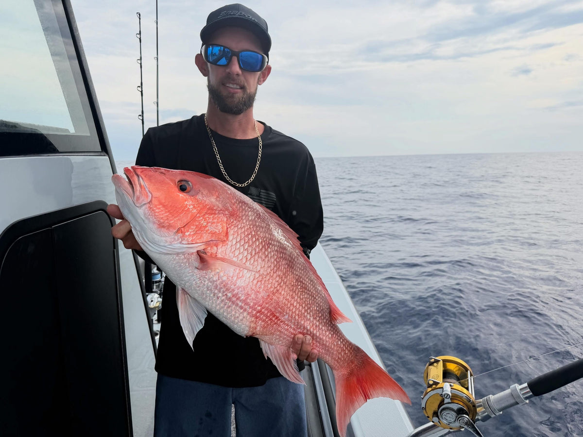 Man holding a large red fish on a DMFD Life Insetta 35IFC Charter Fishing  boat with ocean in the background