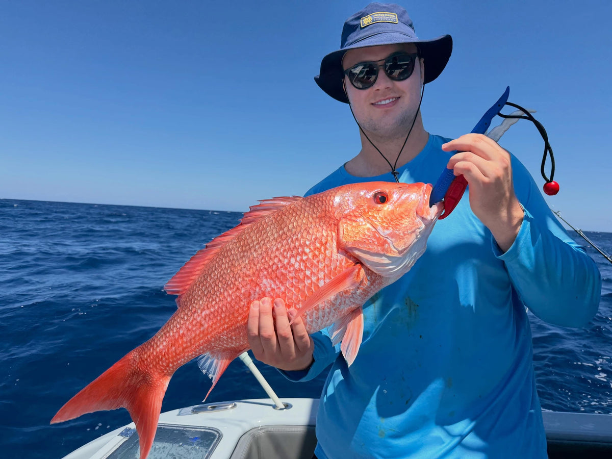 Man holding a large red fish on a DMFD Life Insetta 35IFC Charter Fishing boat with clear blue sky and water.