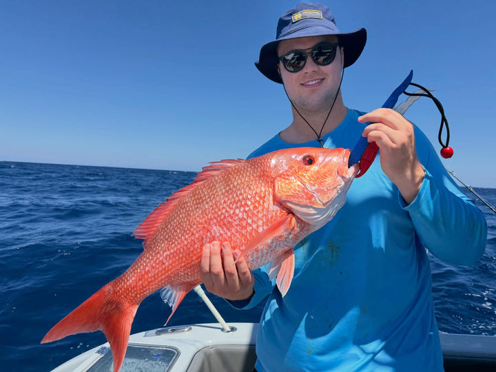Man holding a large red fish on a DMFD Life Insetta 35IFC Charter Fishing boat with clear blue sky and water.