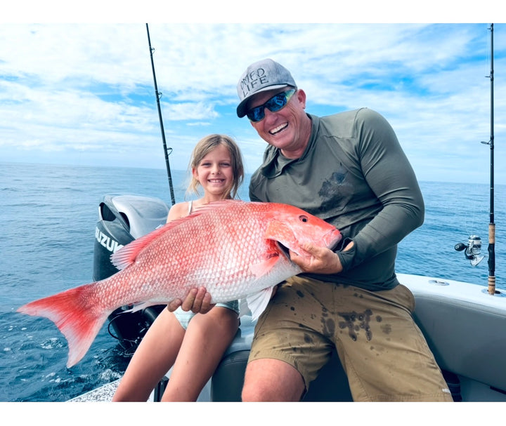 Robert Arrington and child on a Insetta 35 IFC catamaran from DMFD Life Charters holding a large red fish with ocean and sky in the background